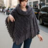 Model in a luxurious blue iris knit mink fur poncho with fringe detailing, posing confidently on a bustling city street.