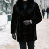 A man modeling a mid-length Black Diamond Cut genuine mink stroller coat with a plush black fox fur collar.