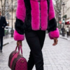 A model wearing a striking black and bright fuchsia fox fur jacket with a voluminous collar.