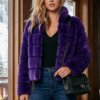 Woman modeling a vibrant purple horizontal cut genuine mink jacket with a black top, blue jeans, and boots in a rustic cabin setting.