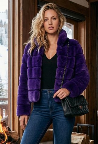 Woman modeling a vibrant purple horizontal cut genuine mink jacket with a black top, blue jeans, and boots in a rustic cabin setting.