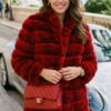 Smiling woman wearing a plush, horizontal-paneled red rex rabbit fur stroller coat with a matching red quilted chain strap handbag, posed outdoors next to a sports car.